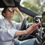 Woman drives car with broken air conditioning in hot Georgia summer weather. She wipes sweat off her forehead with a paper napkin.