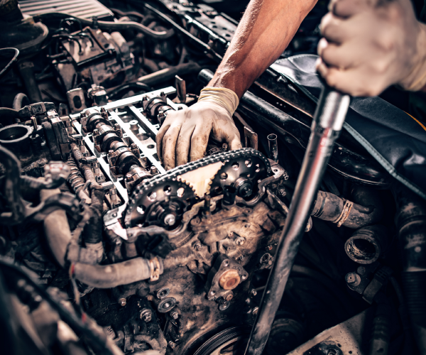 Alpharetta, GA auto technician working in a car under the hood, repairing an engine using a metal tool