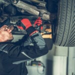 Mechanic upgrading and adjusting suspension system for European vehicle using a large metal wrench.
