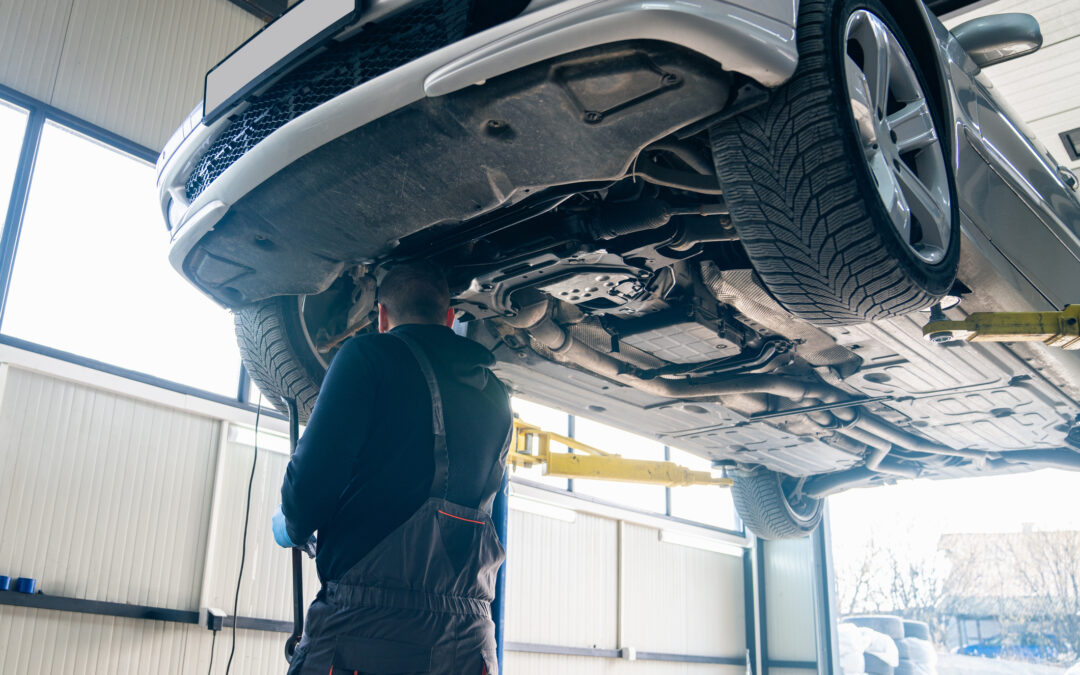 Serviceman checks drive train on a column lift in car service.