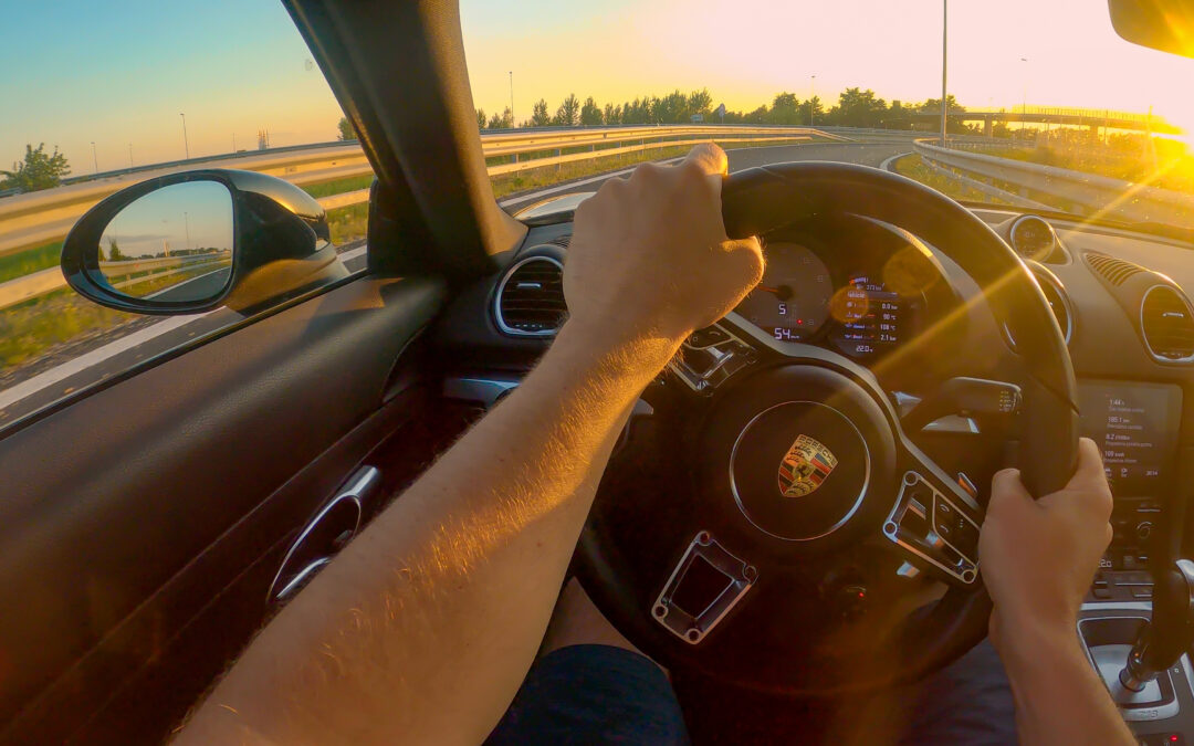 First person view driving a Porsche down the highway at sunset.