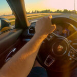 First person view driving a Porsche down the highway at sunset.