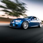 Blue BMW M3 driving on the road with a clear sky overhead